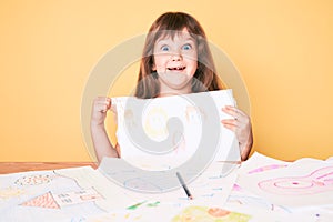 Little caucasian kid girl with long hair drawing colorful paintings pointing thumb up to the side smiling happy with open mouth