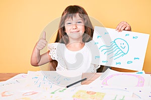 Little caucasian kid girl with long hair drawing colorful paintings smiling happy and positive, thumb up doing excellent and