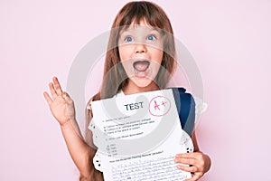 Little caucasian kid girl with long hair showing a passed exam from primary school doing ok sign with fingers, smiling friendly