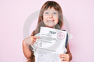 Little caucasian kid girl with long hair showing a passed exam from primary school smiling happy pointing with hand and finger