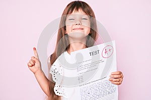 Little caucasian kid girl with long hair showing a passed exam from primary school smiling with an idea or question pointing