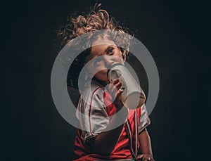 Little champion boy in sportswear with a gold medal drinking water from a bottle. on a dark textured background