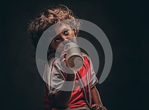 Little champion boy in sportswear with a gold medal drinking water from a bottle. on a dark textured background