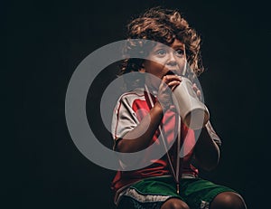 Little champion boy in sportswear with a gold medal drinking water from a bottle. on a dark textured background