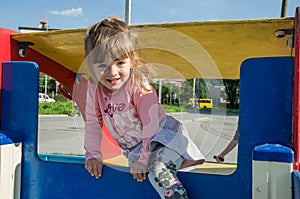 Little charming baby girl playing on a playground, riding on a swing on a bright sunny day