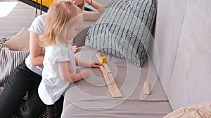 Little charming blond girl playing wood blocks with her mom on the sofa. Road from wood blocks.