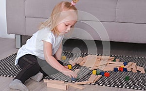 Little charming blond girl playing wood blocks sitting near the sofa.