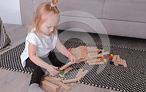 Little charming blond girl playing wood blocks sitting near the sofa.