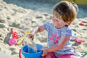 Little charming girl baby playing on the playground in the sandbox sand mound in the bucket with a shovel and rake