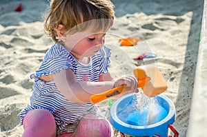 Little charming girl baby playing on the playground in the sandbox sand mound in the bucket with a shovel and rake