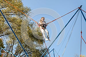 Little charming girl child on elastic ropes jumps on a trampoline in an amusement park