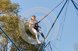 Little charming girl child on elastic ropes jumps on a trampoline in an amusement park