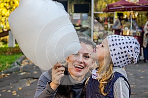 A little charming girl with her mama is eating huge cotton candy in an amusement park - a happy family