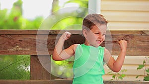 The little cheerful boy in a green t-shirt is showing bicep muscles