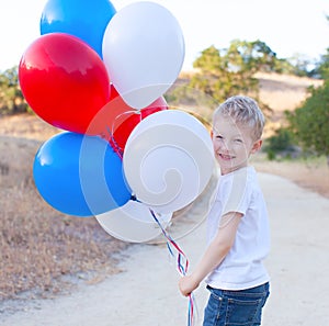 little cheerful boy holding colorful balloons and celebrating 4th of July