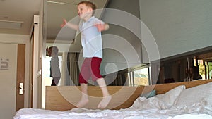 A little cheerful boy jumps on the bed in the morning. Slow motion.