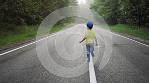 Little cheerful boy runs along the center of the road in the forest after rain. Back view. Slow motion