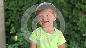 The little cheerful boy in a t-shirt is showing bicep muscles outdoors