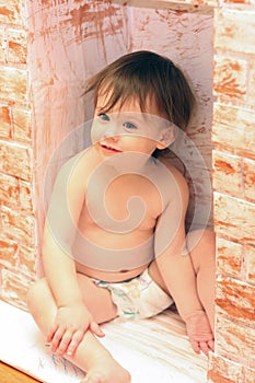 Little cheerful cute white baby in a diaper sitting in a toy fireplace