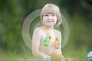 A little cheerful girl in a bright bathing suit on a green lawn on a warm summer day. Beautiful portrait of a charming girl