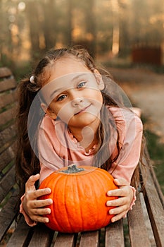 A little cheerful girl holds an orange pumpkin in the park in the autumn. Halloween props