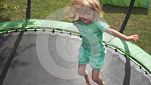 A little cheerful girl is jumping on the trampoline in the backyard