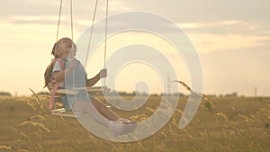 Little cheerful girl laughs, rejoices in flight on a swing. healthy happy child rides on a rope swing on branch in park