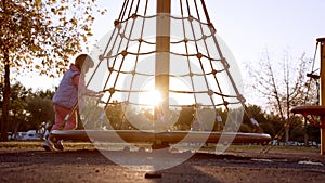 little cheerful girl in pink tracksuit plays on playground and spin on carousel against backdrop of setting sun in city