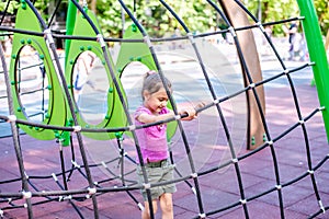 Little cheerful girl plays on vacation in the park at the playground. The child is having fun on the street on vacation.