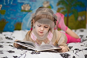 Little cheerful girl read book in bed