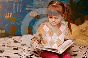 Little cheerful girl read book in bed