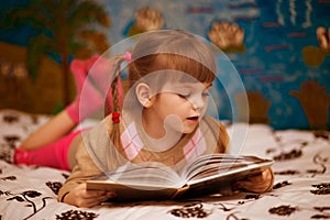 Little cheerful girl read book in bed
