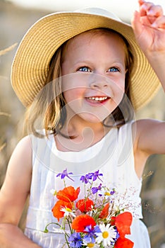 Little cheerful girl in a straw hat with wild flowers red poppy bouquet