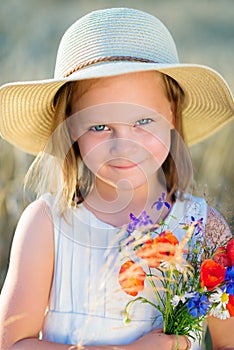 Little cheerful girl in a straw hat with wild flowers red poppy