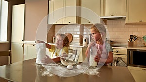 Little chefs. Two cute children, boy and girl in aprons adding ingredients while cooking, preparing dough together on