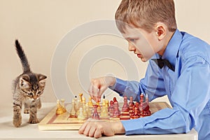 Little chessplayer with playful kitten plays chess.