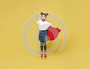 Little child asian girl plays superhero on yellow background studio shot. Girl power hero concept