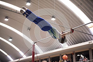 Little child athletic gymnast performing exercises at the bar in the championship