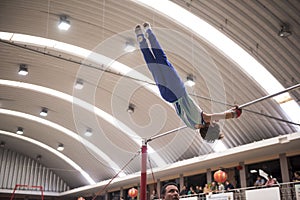 Little child athletic gymnast performing exercises at the bar in the championship