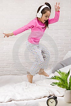 Little girl listening to the music with the headphones on bed.