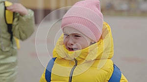 a little child with a backpack is crying in his mother's arms, tears are rolling down kid's face, little girl is upset