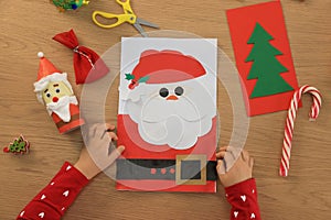 Little child with beautiful Christmas greeting card at wooden table, top view