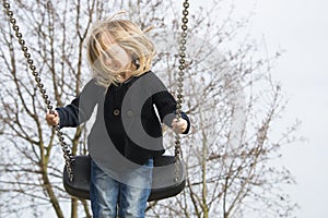 Little child blond girl having fun on a swing outdoor.