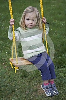 Little child blond girl having fun on a swing outdoor. Summer playground