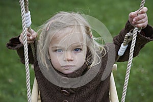 Little child blond girl having fun on a swing outdoor. Summer playground