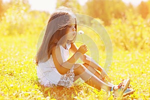 Little child blowing dandelion in sunny summer day