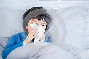 Little child boy blow his nose. Sick child with napkin in bed. Allergic kid, flu season. Kid with cold rhinitis, get cold