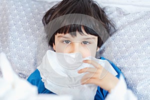 Little child boy blow his nose. Sick child with napkin in bed. Allergic kid, flu season. Kid with cold rhinitis, get cold