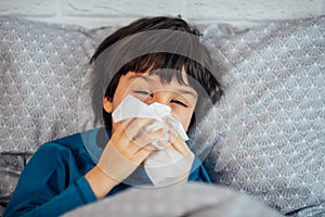 Little child boy blowing his nose. Sick child with napkin in bed