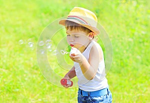 Little child boy blowing soap bubbles outdoors in summer